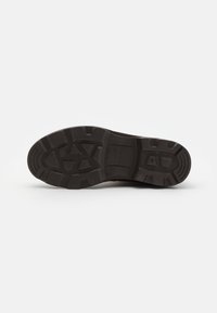 Suola di scarpa in gomma nera con una superficie testurizzata, caratterizzata da scanalature a motivo per una migliore aderenza e una forma della punta arrotondata. Marchi del brand ben visibili.