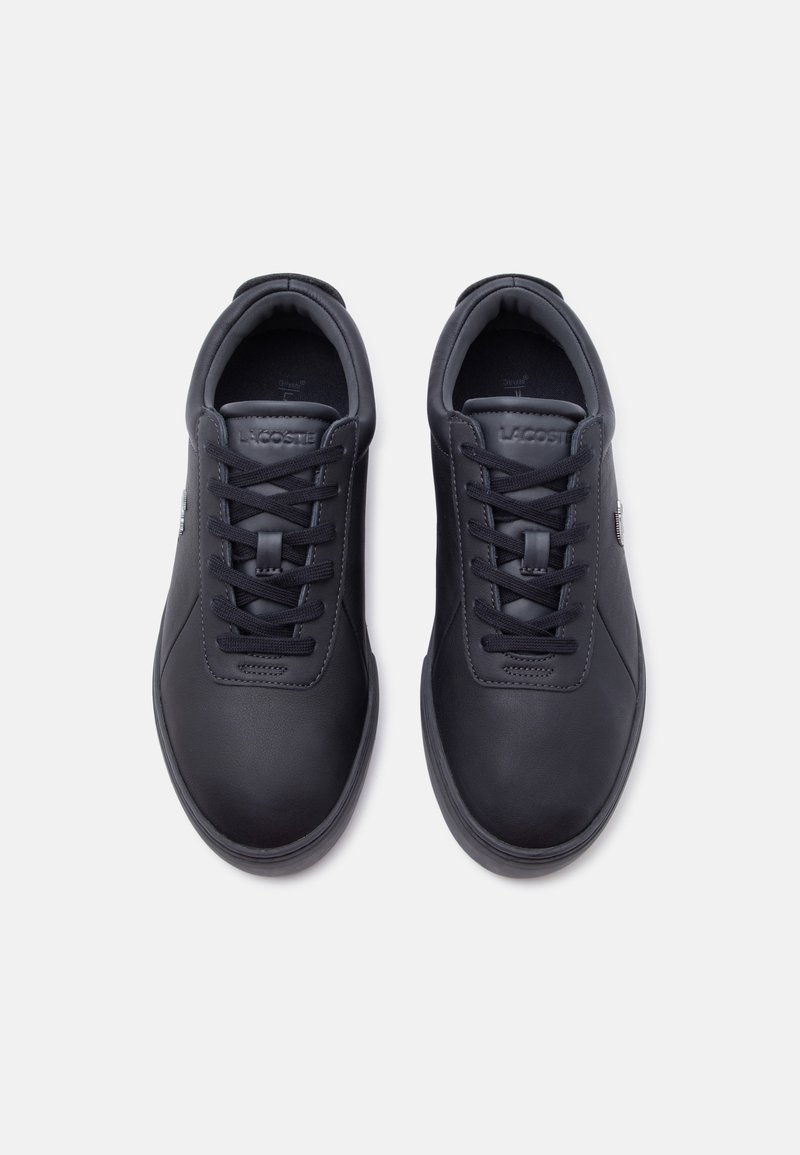 Een paar zwarte Lacoste sneakers met veters, gezien van bovenaf op een witte achtergrond.