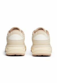 Chaussures de sport beiges avec un design texturé, un col rembourré et des semelles amorties. Les caractéristiques comprennent un logo discret sur le talon et des surfaces lisses.