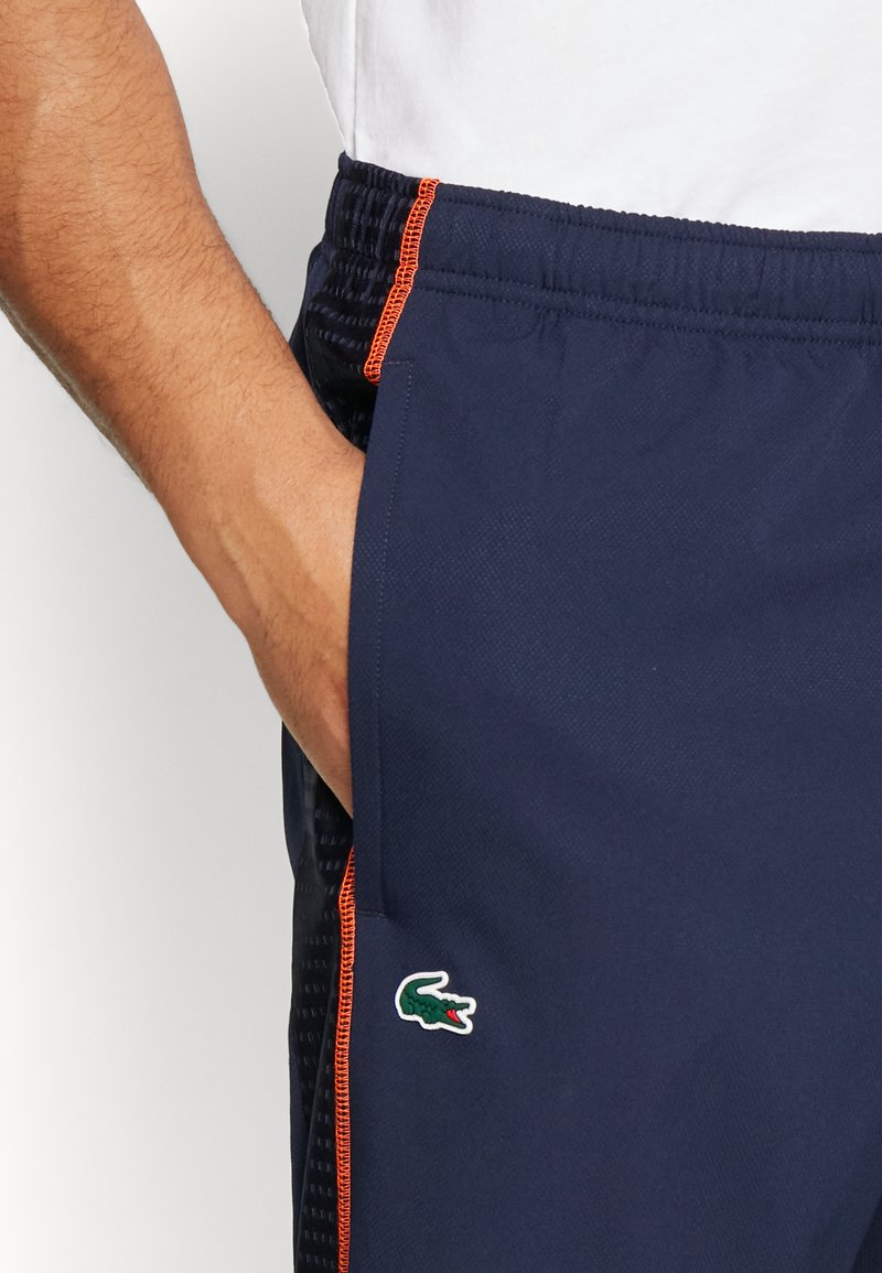 Marine korte broek van lichtgewicht stof, met oranje stiksels, zijzakken en een groene krokodillogo op het onderbeen.