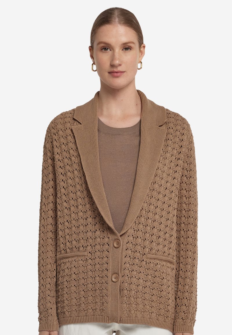 Brun stickad cardigan med ett strukturerat mönster, en v-formad krage, två framfickor och två knappstängningar. Bärs över en matchande topp.
