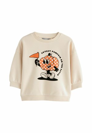 Sweter w kolorze kremowym z okrągłym dekoltem i rękawami w kształcie balonów. Ma grafikę uśmiechniętej dyni trzymającej flagę, z tekstem poniżej.