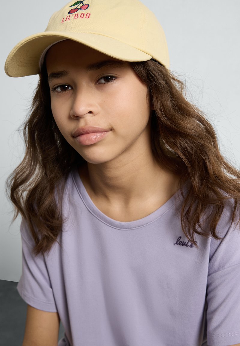 Lila pamut póló kerek nyakkal és rövid ujjakkal, "Levi's" hímzéssel; sárga baseball sapka cseresznye grafikai részletekkel.