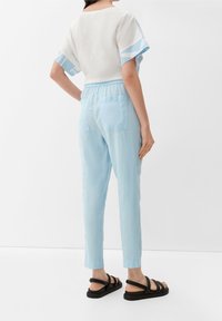 Lichtblauwe joggingbroek met elastische tailleband en twee achterzakken, gecombineerd met een witte top met blauw patroon op de mouwen. Zwarte sandalen.