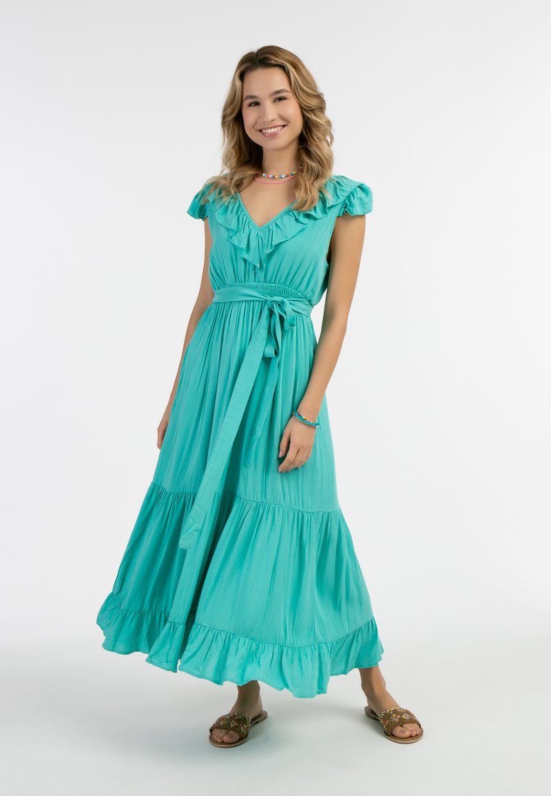 Rochie maxi turcoaz cu mâneci volan, decolteu în V și talie legată. Prezintă un design în straturi și un material moale cu o siluetă fluidă.