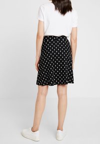 Jupe noire avec un motif en losanges blancs, fabriquée dans un tissu léger, coupe évasée, portée avec un t-shirt blanc et des baskets blanches.