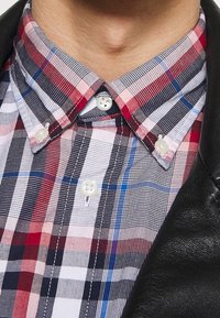 Hemd mit Knopfleiste in einem rot-blau-weißen Karomuster. Verfügt über einen spitzen Kragen und weiße Knöpfe, kombiniert mit einer schwarzen Lederjacke.