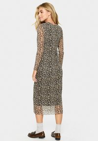 Lång leopardmönstrad klänning med genomskinliga långärmar, figurnära siluett och midi-längd. Har en rund halsringning och mjuk textur.