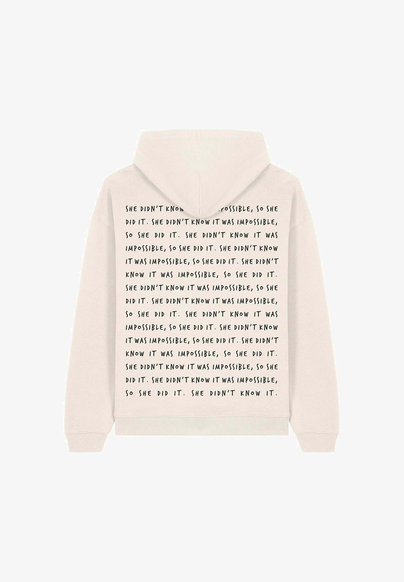Un sweat à capuche beige clair avec une poche kangourou. Le dos présente un texte noir répété : "Elle ne savait pas que c'était impossible, alors elle l'a fait."