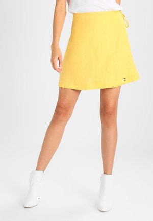 Yellow linen A-line mini skirt with a tie waist, featuring a small heart embroidery detail near the hem. Smooth texture and lightweight design.