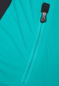 Un primer plano de una tela turquesa con un zipper negro y una pestaña texturizada, destacando la superficie suave y los detalles de las costuras.