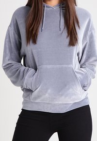 Šedá oversized mikina vyrobená z měkké, plyšové látky. Obsahuje velkou přední kapsu, nastavitelné šňůrky a žebrované manžety.