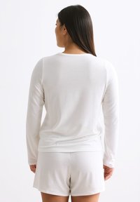 Weißes Langarmshirt mit Rundhalsausschnitt, kombiniert mit weißen Shorts. Weicher Stoff mit glatter Textur, minimalistisches Design und keine sichtbaren Muster.