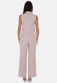 Blazer senza maniche di colore rosa chiaro e pantaloni a gamba larga, realizzati in tessuto morbido. Presenta una vestibilità su misura e dettagli di cucitura discreti.