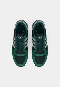 Green and black athletic shoes with grey accents, featuring a textured fabric upper, three white stripes, and a round toe design.