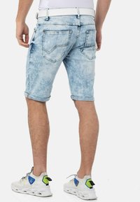 Hellblaue Jeansshorts mit einer verblassten Wäsche, aufgerollten Säumen und zwei Gesäßtaschen mit Stickdetails. Getragen mit weißen Sneakers.