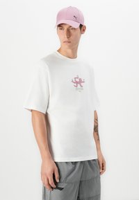 White cotton t-shirt with short sleeves, featuring a pink graphic design and green text. Complemented by a light pink cap, made of similar material.