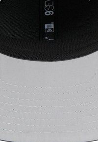 Gorra estructurada con una parte frontal gris, visera negra con textura y detalles de costura blanca. Presenta una etiqueta del fabricante en el interior, que indica la talla.