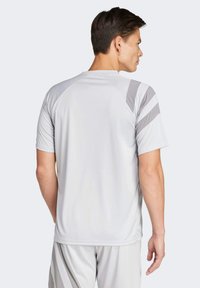 Lichtgrijze sportshirt met korte mouwen en raglanontwerp. Heeft grijze strepen op de schouders. Gladde, vochtafvoerende stof.