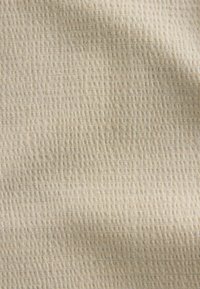 Tissu beige avec un motif gaufré texturé en petits carrés et des ombres subtiles indiquant des plis doux.