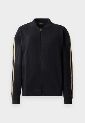 Zwarte zip-up jack met beige strepen op de mouwen, geribbelde manchetten en kraag, en een gouden rits, weergegeven op een witte achtergrond.