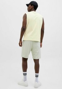 Haut sans manches jaune clair associé à un short vert clair. Modèle portant des baskets blanches avec des chaussettes rayées noires. Design simple et décontracté.