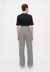 Black short-sleeve top paired with high-waisted, wide-leg pants featuring horizontal black and white stripes. Model wears light gray shoes.