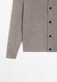Szary dziergany kardigan z zapięciem na guziki, prążkowanymi mankietami i gładką fakturą. Tkanina ma subtelny melanż.