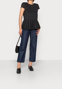 Top peplum negro con mangas cortas, con rayas verticales, combinado con vaqueros de pierna ancha de color azul oscuro y mocasines negros. Se incluye un bolso pequeño.