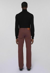Schwarzer Rollkragenpullover kombiniert mit burgunderfarbenen Hosen. Die Hosen haben ein Lederetikett am Bund und ein gerades Bein-Design. Schwarzes Schuhwerk sichtbar.