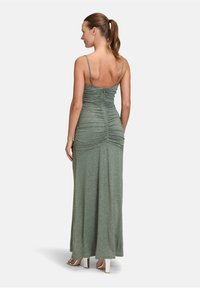 Dopasowana sukienka o długości maxi w stonowanej zieleni z marszczeniami. Posiada cienkie ramiączka i błyszczące wykończenie. Gładka tekstura, długość do kostek.