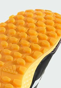 Czarna podeszwa sportowego buta z teksturowanym żółtym gumowym uchwytem, z sześciokątnymi wzorami i widocznymi rowkami dla lepszej przyczepności.