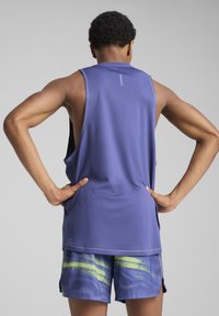 Canotta atletica viola senza maniche con una vestibilità ampia, realizzata in tessuto leggero, abbinata a pantaloni corti a fantasia con strisce verdi e blu.