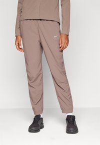 Nike joggingbroek in een gedempte bruine stof heeft een elastische tailleband, taps toelopende benen en een klein wit logo op de linker bovenbeen.