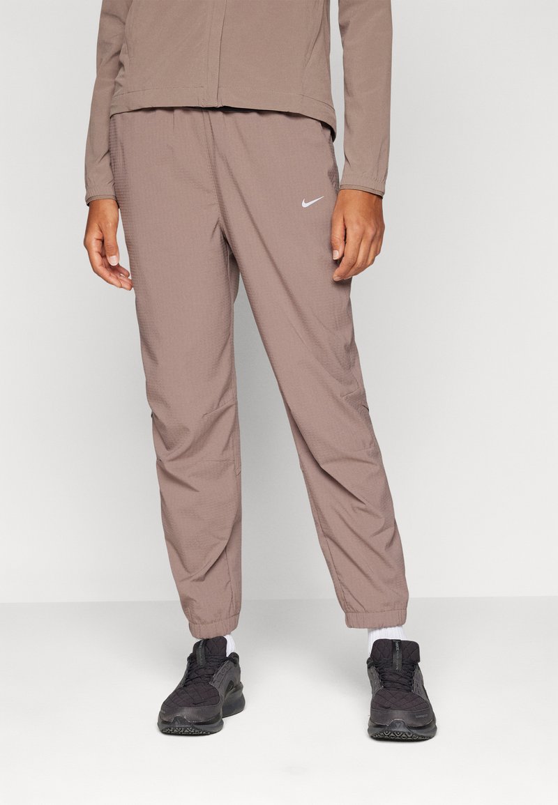 Nike joggingbroek in een gedempte bruine stof heeft een elastische tailleband, taps toelopende benen en een klein wit logo op de linker bovenbeen.