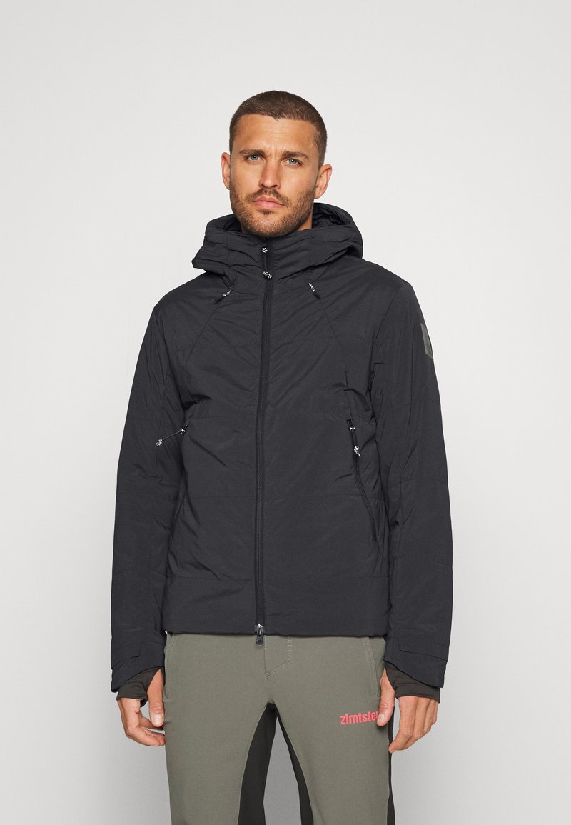 Veste à capuche noire avec une finition texturée, fermeture éclair sur le devant et deux poches zippées. Comprend des cordons réglables au niveau de la capuche.