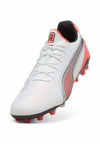 Botín de fútbol blanco con acabado suave, con acentos naranjas, un panel lateral texturizado y una suela negra con tachuelas rojas.