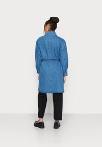 Płaszcz dżinsowy z paskiem w talii, długimi rękawami i bocznymi kieszeniami. Materiał w średnim odcieniu niebieskiego, o strukturalnym, lekko oversize'owym kroju.