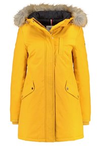 Gul parka med en fuskpälsfodrad huva, dragkedja och tryckknappar, två framfickor och elastiska ärmslut. Tillverkad av ett hållbart och väderbeständigt tyg.