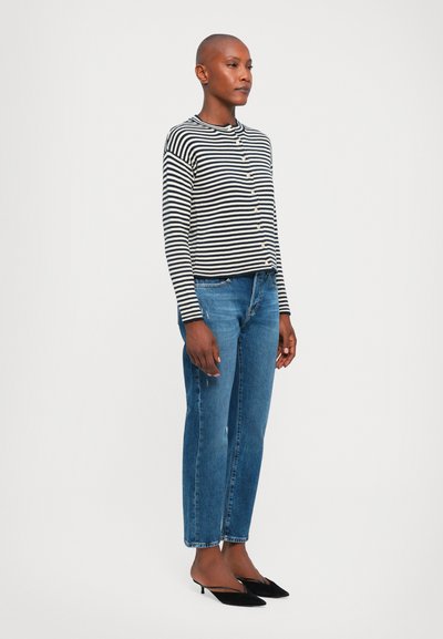 Gestreifter Langarm-Cardigan in Schwarz und Weiß, mit Knopfleiste, kombiniert mit blauen gerade geschnittenen Jeans und schwarzen Kitten Heels.