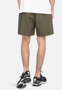 Olijfgroene shorts van een lichtgewicht stof, met een relaxte pasvorm en een elastische tailleband. Gecombineerd met zwarte sportschoenen met witte accenten.