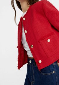 Rode cropped jack gemaakt van textuurstof met rafelige randen, voorzien van gouden knopen en een voorzak, gedragen over een witte top.