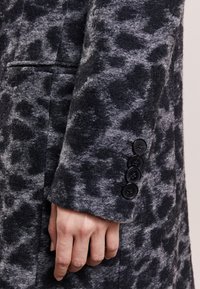 Wollen jas met een zwart- en grijsleeuwprint, zijzak en vier zwarte knopen op de manchetten voor detail.