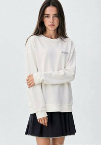 Krémový svetr s volným střihem, vroubkovanými manžetami a drobnými švy. V kombinaci s černou skládací sukní.