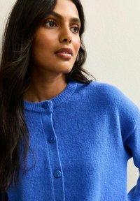 Koninklijk blauwe wollen cardigan met een ronde halslijn en ribbelrand. Voorzien van twee knopen aan de voorkant en een zachte, gestructureerde stof.