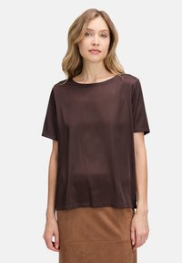 T-shirt marron à manches courtes avec un col rond, texture lisse et coupe décontractée, associé à une jupe en daim beige.