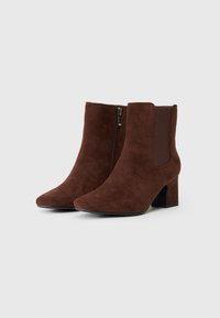 Bottines en daim marron avec un bout pointu, fermeture éclair sur le côté, panneaux latéraux élastiques et un talon épais. Semelle noire plate.