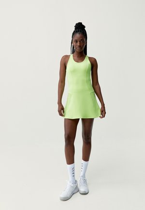Racerback dress in bright green, made of smooth fabric. Features a flared skirt with mesh side panels. Paired with white sneakers and socks.