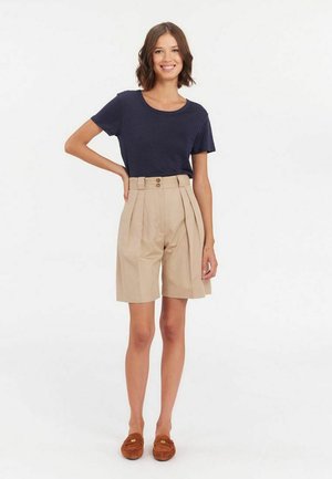 T-shirt bleu marine avec un col rond, associé à un short beige plissé avec une taille haute et deux boutons sur le devant.