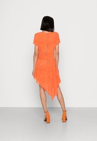 Vestido laranja assimétrico com mangas curtas, tecido texturizado e costas com recorte em formato de buraco chave. Combinado com sandálias de salto bloco a condizer.